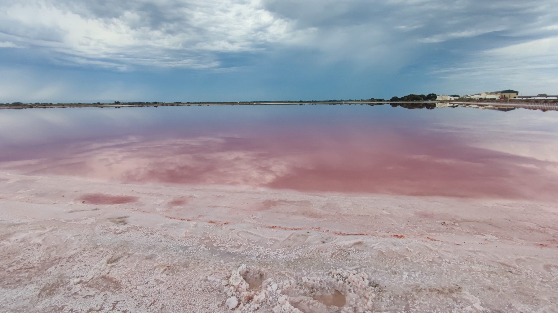 Lagune salée aux reflets roses sous un ciel nuageux en France