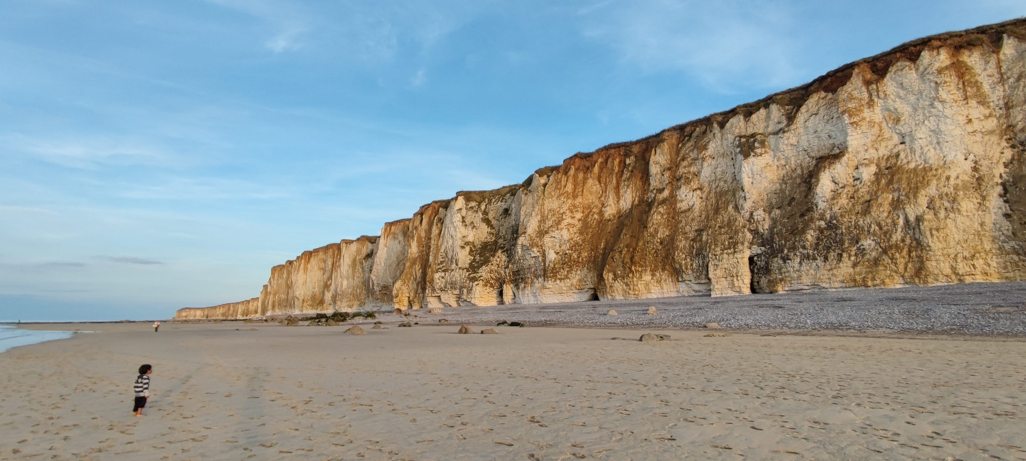 Enfant marchant sur une plage au pied de hautes falaises